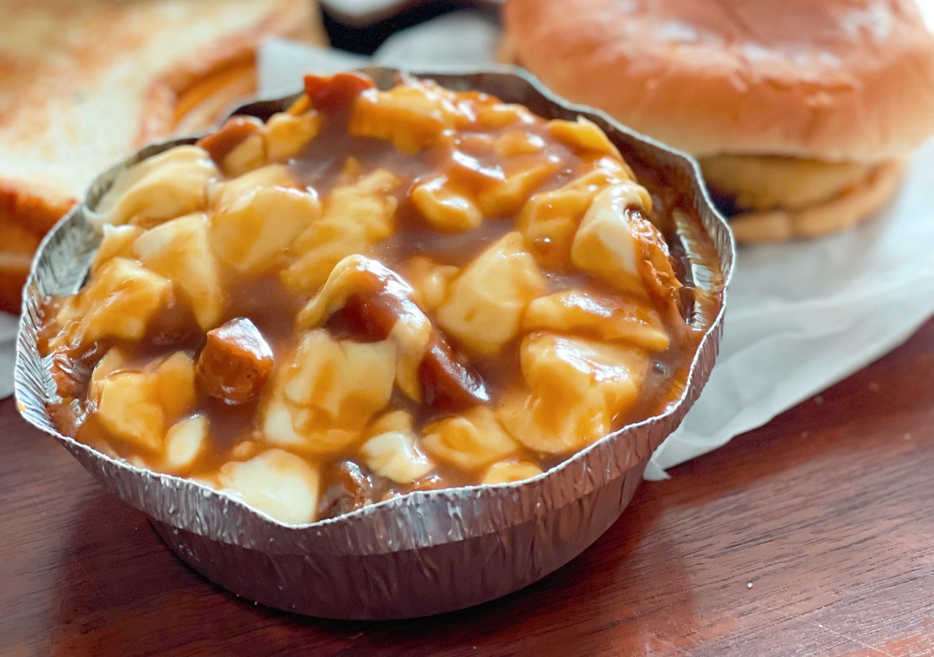 Best Poutine in Quebec City: Poutine in a round foil pan, a burger and grilled cheese sandwich in the background.